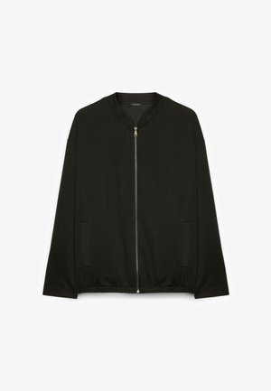 Veste noire à manches longues avec fermeture éclair, petit motif à pois discret, poches latérales, ourlet élastique et col rond.