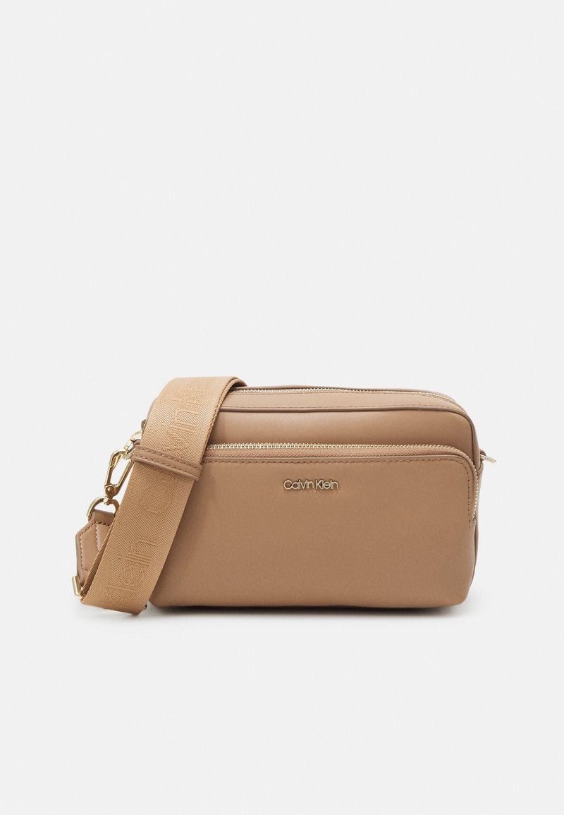 Taninová crossbody taška vyrobená z hladké umělé kůže. Má zipovou kapsu a nastavitelný popruh s embosovanými logovými akcenty. Zlaté kovové detaily.