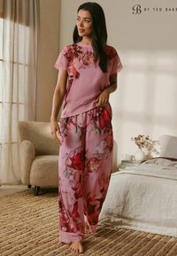 Ružový pyžamový set zahŕňajúci vrch s kvetinovým vzorom a čipkovanými rukávmi a zodpovedajúce voľné nohavice s kvetinovými akcentmi. Mäkká, ľahká látka.