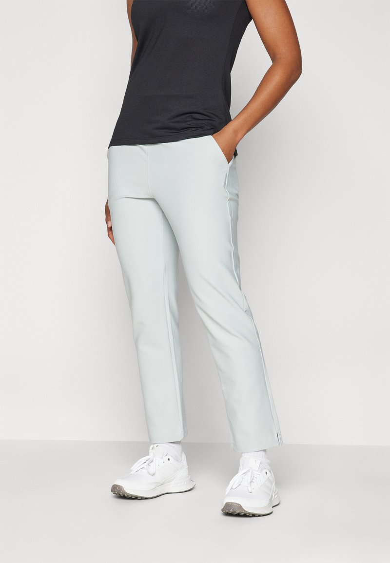 Calças cortadas em azul claro, com bolsos laterais e uma textura suave, combinadas com uma blusa preta ajustada e sapatos de desporto brancos.