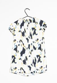 Blouse à manches courtes avec une coupe ample, motif abstrait multicolore en noir, blanc, jaune, bleu et vert clair, suspendue sur un cintre noir.