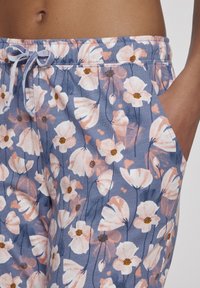 Bloemrijke joggingbroek in het blauw met roze en bruine bloemen. Beschikt over een elastische tailleband met een trekkoord en zijzakken.