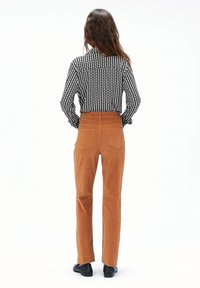 Pantalones de pana marrones con piernas rectas, cintura alta y dos bolsillos traseros. Combinados con una camisa de patrón en blanco y negro. Se ven zapatos negros.