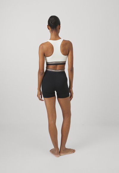 Senza maniche bianca sportiva con design racerback e branding nero; abbinata a pantaloni corti neri aderenti, entrambi realizzati in tessuto elasticizzato.