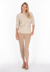 Pulover bej din tricot cu un model texturat, deschis, și mâneci scurte, asortat cu pantaloni bej tapered și tocuri nude.