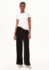 T-shirt blanc à manches courtes associé à un pantalon large noir et des baskets rayées. Tissu lisse avec un design décontracté et détail de label sur le côté.
