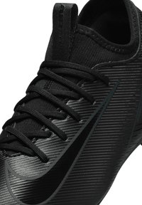 Svart sportskor med en texturerad syntetisk ovandel, med platta svarta snören, rund tå och en subtil swoosh-detalj.