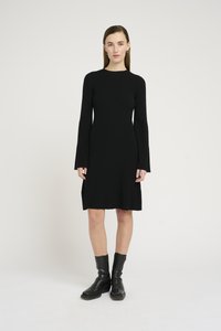 Black rib-knit dress with long sleeves, featuring a fitted silhouette and slits at the hem. Worn with black leather ankle boots.