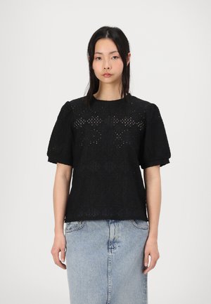 Black lace blouse with short puff sleeves, pattern of cut-out details, round neckline, paired with a light blue denim skirt.