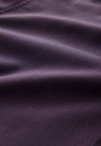 Dunkellila Stoff mit glatter Textur, feiner Rippung und subtiler Glanz, gefaltet, um den Fall und die weiche Oberfläche zu zeigen.