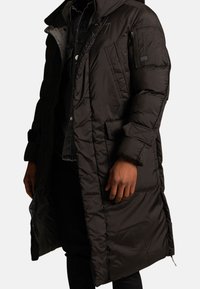 Czarna puchowa kurtka o długim kroju, zapinana na zamek, pikowana, z wieloma kieszeniami. Posiada kaptur i elastyczne mankiety.