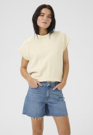 Light cream t-shirt with short sleeves, featuring a subtle embossed design, paired with blue denim shorts having frayed hems.