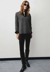 Maglione grigio glitterato con scollo a V, indossato sopra una camicia nera. Abbinato a pantaloni neri aderenti e stivali neri al ginocchio con zip.