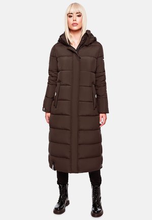 Bruine pufferjas met een capuchon, met horizontaal gestikte secties, zijzakken en drukknoopdetails. Draagt over zwarte broek en laarzen.