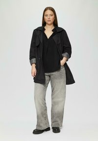 Czarny płaszcz trench z szarymi akcentami, dopasowana czarna bluzka, szare dżinsy z szerokimi nogawkami oraz masywne czarne botki. Gładka tekstura; casualowy design.