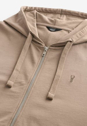 Beige Zip-Hoodie aus weichem Stoff mit einheitlicher Textur. Verfügt über eine Kordelzugkapuze, einen silbernen Reißverschluss und ein kleines gesticktes Logo.