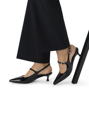 Zwarte gepatenteerde leren slingback hakken met een spitse neus, verstelbare band en een smalle, gemiddelde hak. Glad, glanzend oppervlak.