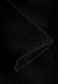 Telas negras con una superficie suave y texturizada, que presenta un sutil patrón acanalado y un pliegue en ángulo que destaca su grosor y sensación acogedora.
