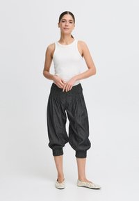 Pantalons noir smockés à longueur de cheville avec une coupe ample et des poignets froncés, associés à un haut sans manches blanc et des ballerines à motifs légers.
