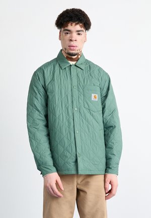 Chaqueta verde acolchada con cuello tipo solapa, botones en la parte delantera y un bolsillo en el pecho izquierdo con un logo. Está hecha de un material suave y ligero.