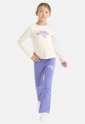 Camicia color crema a maniche lunghe e pantaloni viola con logo "Diadora". Tessuto di cotone liscio, design aderente, abbinati a scarpe da ginnastica bianche.