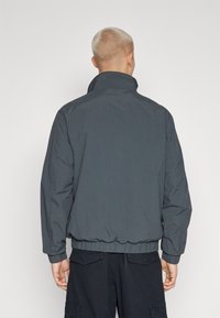 Chaqueta de plumas gris oscuro con cuello alto y puños y dobladillo elásticos, con una textura suave y un diseño minimalista.