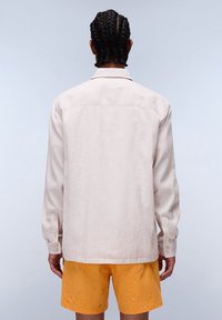 Beige corduroy shirt with long sleeves and a back yoke, featuring a collared neck and buttoned cuffs, worn with bright yellow shorts.