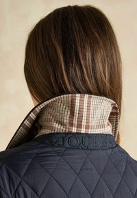 Granatowa pikowana kurtka z kołnierzem, wewnątrz wyłożona brązowym i beżowym wzorem w kratę. Na zewnętrznej stronie kołnierza wyszyto "JOULES".