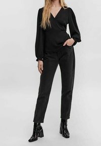 Czarna bluzka o kroju wrap z długimi, bufiastymi rękawami, zestawiona z czarnymi dżinsami z wysokim stanem oraz błyszczącymi botkami na obcasie. Prosty, elegancki design.