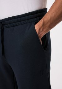 Pantalones de chándal azul marino con cintura elástica y cordón; cuentan con bolsillos laterales y una tela texturizada con un pequeño logo.
