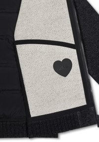 Interno della giacca nero e grigio chiaro con un tessuto grigio chiaro texturizzato, dettagli neri e un'etichetta a forma di cuore con la scritta "Fatto con amore."
