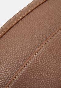 Cuir marron texturé avec une finition en relief, présentant des coutures contrastantes couleur tan et des éléments de design arrondis. Aucun détail en métal visible.
