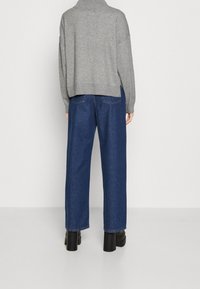 Pull gris surdimensionné avec un col haut et des fentes latérales ; associé à un jean en denim bleu foncé à jambes larges et des bottines noires.
