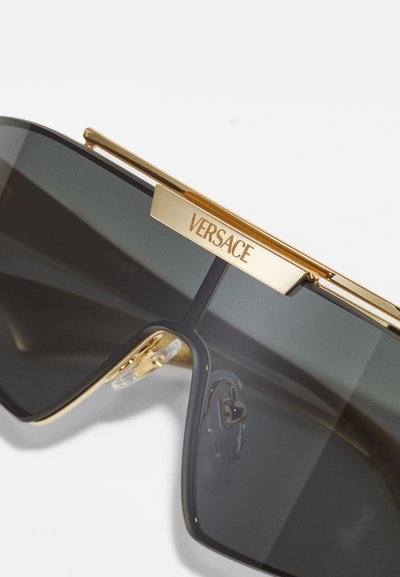 Sončna očala imajo velike sive leče z zlatim kovinskim okvirjem. Na vrhu je dodan zlat trak z napisom "VERSACE". Vključeni so prozorni nosni blazinici.