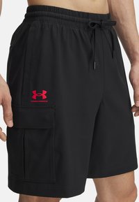 Bañadores negros de tejido ligero, con cintura elástica, cordón ajustable, bolsillo lateral y un logo rojo de Under Armour.