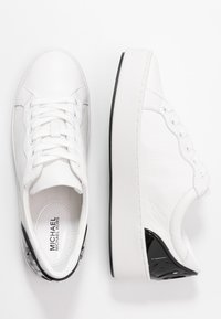 Baskets en cuir blanc avec une finition texturée, dotées d'un bout lisse, d'un laçage et d'un accent noir au niveau du talon.