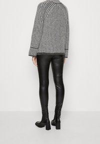 Grijze en zwarte gestreepte gebreide trui met hoge kraag, gecombineerd met glanzende zwarte leggings en zwarte blokhak enkellaarsjes.