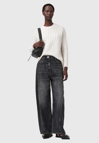 Maglione crema a trecce, jeans neri a vita alta con gamba ampia, borsa a tracolla nera e scarpe nere flat. Dettaglio floreale sottile sui jeans.