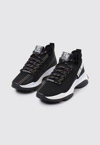 Chaussures de sport noires en maille respirante avec des détails texturés, semelle blanche contrastante et lacets colorés. Logo notable sur la languette.