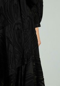 Schwarzes, strukturiertes Kleid mit komplexen floralen Mustern, fließendem Stoff und langen Ärmeln; ausgestattet mit einem geschichteten Design und weichem Finish.