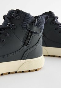 Bottines gris foncé avec un col texturé, fermeture éclair sur le côté et semelle en caoutchouc de couleur claire présentant un motif de traction.