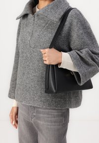 Suéter de lana gris con cuello alto y cremallera hasta el pecho, combinado con un bolso de cuero negro con forma estructurada y correa corta.
