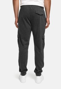 Gray sweatpants with a relaxed fit, two side cargo pockets, and a drawstring waistband, paired with white sneakers.
