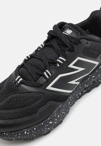 Black athletic shoe with a textured mesh upper, reflective accents, and a speckled rubber sole. Features traditional lace-up design.