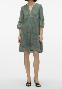 Robe en dentelle de couleur vert doux avec un décolleté en V, des manches trois-quarts et un design à étages. Comprend des motifs complexes et une doublure fluide.