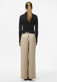 Melnā piegu�ļošā garroku krekla, bēšu platu biksu un spīdīga melna josta ar ikdienišķiem melniem apaviem attēlojums no aizmugures.