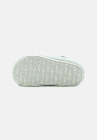 Sula på en ljusgrön Crocs-sko med en mjuk textur, med ett upprepat "crocs"-logotypmönster och en konturerad, rundad form.