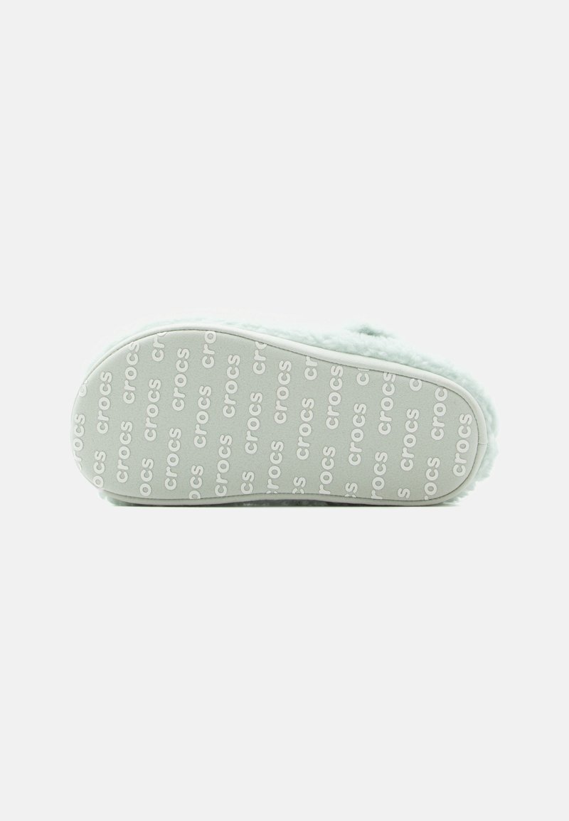 Suela de un zapato Crocs de color verde claro con una textura suave, con un patrón repetido del logo "crocs" y una forma contorneada y redondeada.