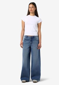 Λευκό κοντομάνικο μπλουζάκι συνδυασμένο με φαρδιά τζιν παντελόνια σε μπλε απόχρωση, που διαθέτουν κλασικό σχέδιο με πέντε τσέπες και ελαφρώς ξεθωριασμένο τελείωμα.