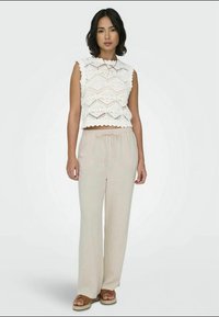 Un crop top en crochet blanc avec un ourlet en dents de scie associé à un pantalon beige clair, ample. Sandales avec une semelle épaisse tressée.